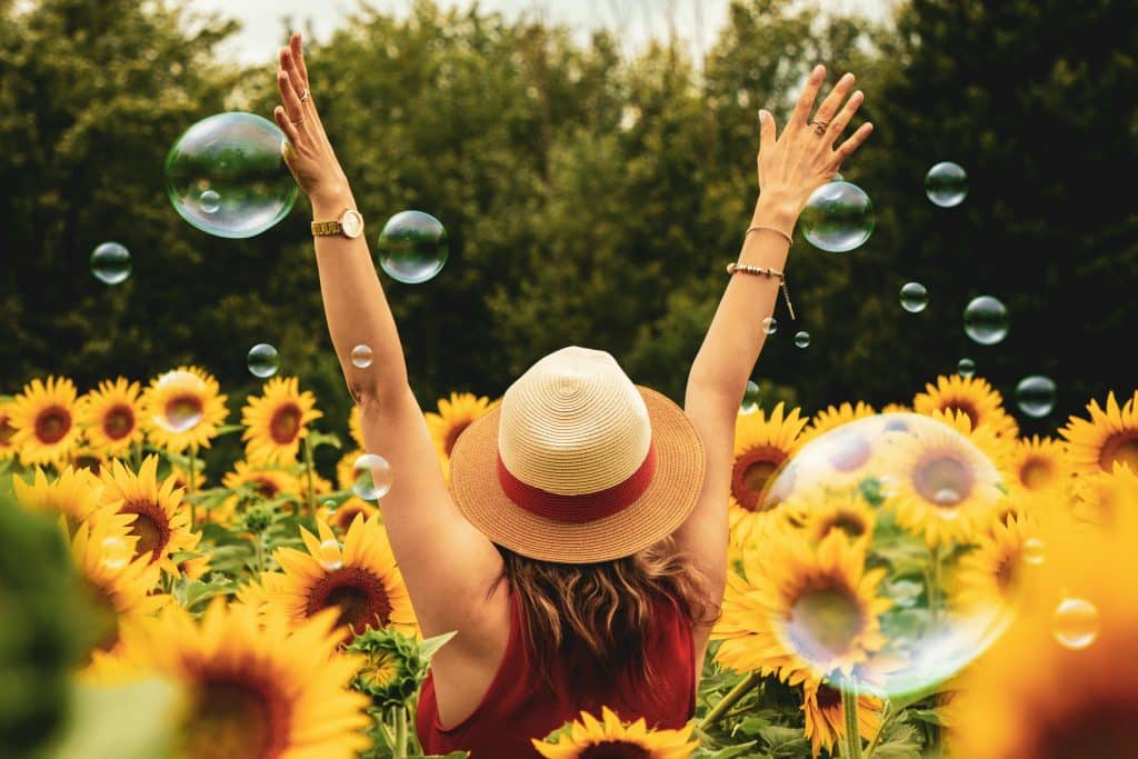 Femme de dos les mains en l'air dans un chant de tournesols, entourée de bulles de savon