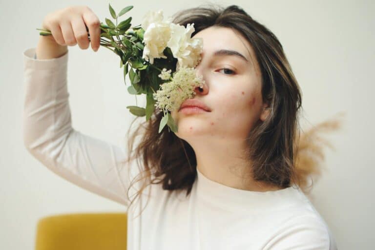 Jeune femme avec quelques boutons d'acné qui se cache une partie du visage avec un bouquet de fleurs