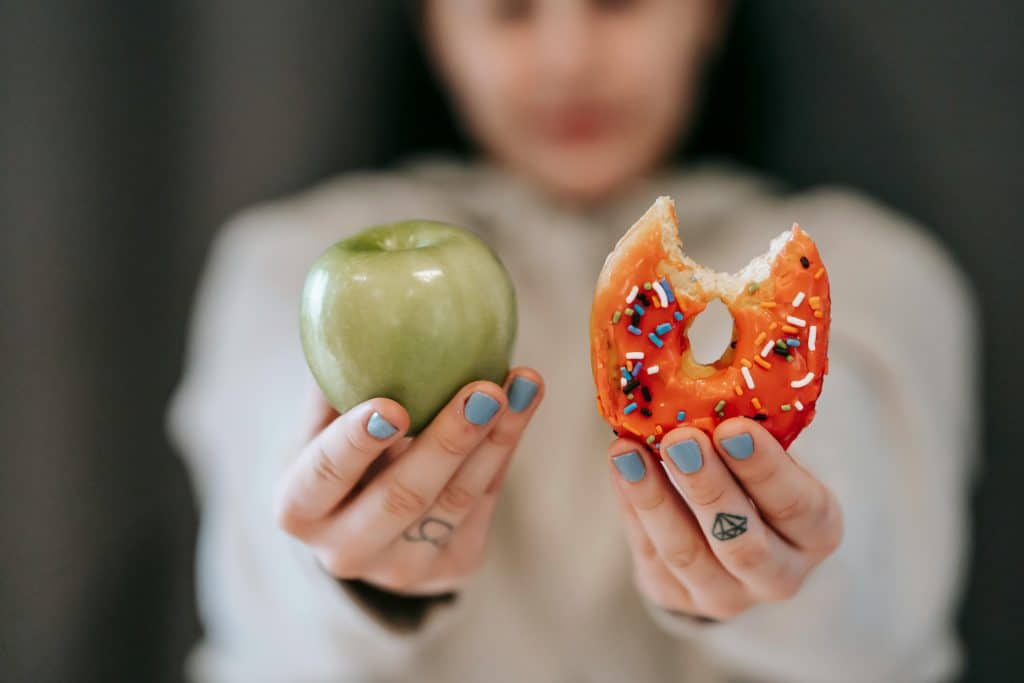 Femme tenant une pomme verte dans sa main droite et un donut dans sa main gauche