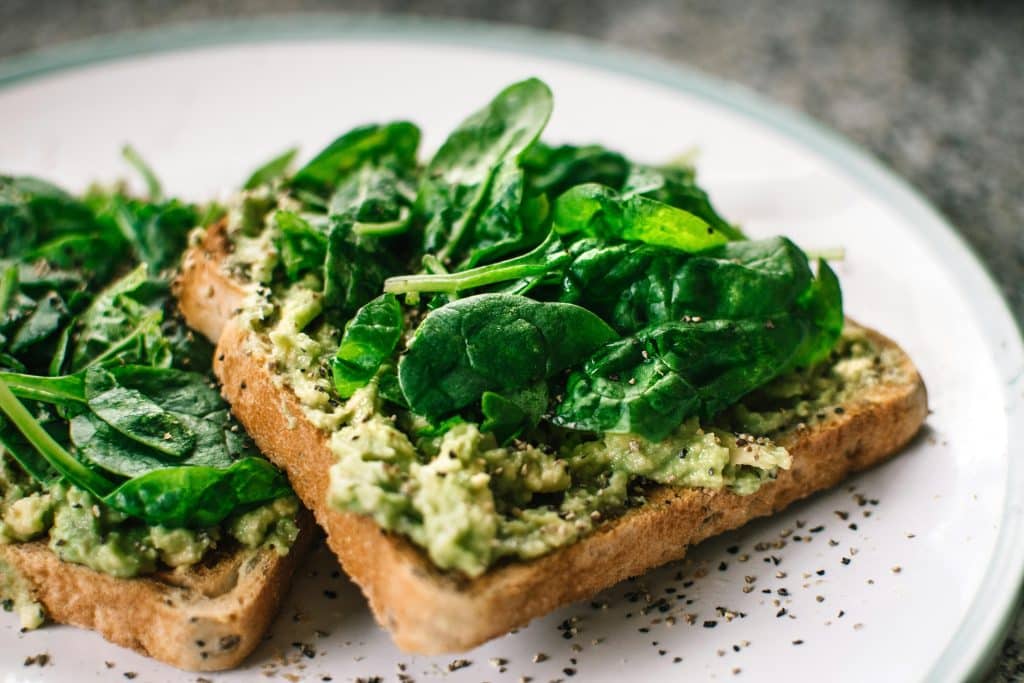 Deux toasts de pain complet avec une purée d'avocat et des feuilles de mâche