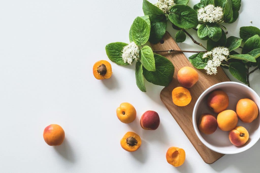 Abricots dans un saladier blanc situé sur une planche à découper en bois avec des feuilles de menthe