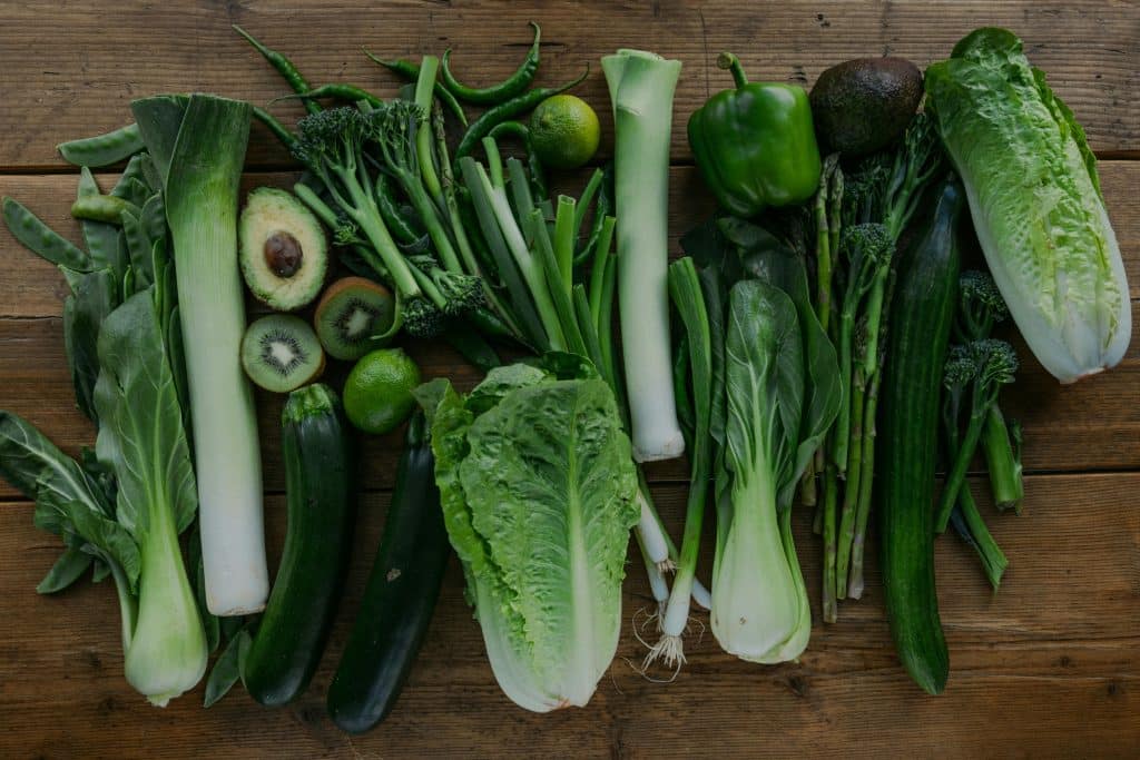 Légumes et fruits verts étalés sur une table : poireaux, poivron, avocat, citron, piment, courgettes, choux, kiwi