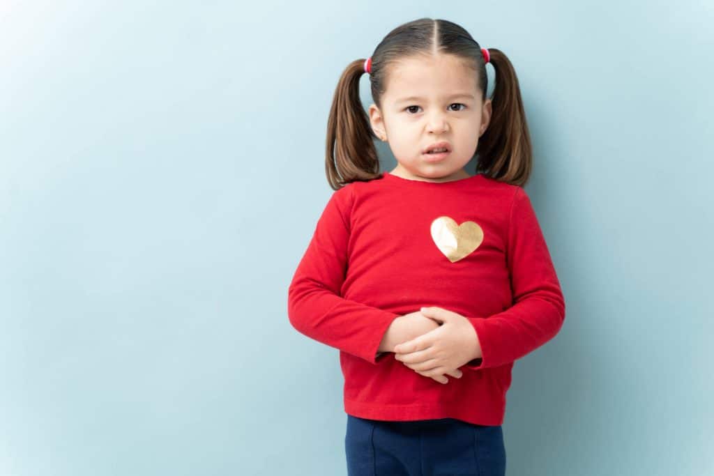 Petite fille qui se tient le ventre en faisant une légère grimace de gêne