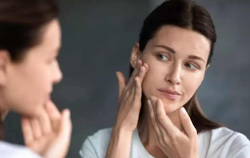 Femme quarantenaire qui inspecte sa peau dans un miroir