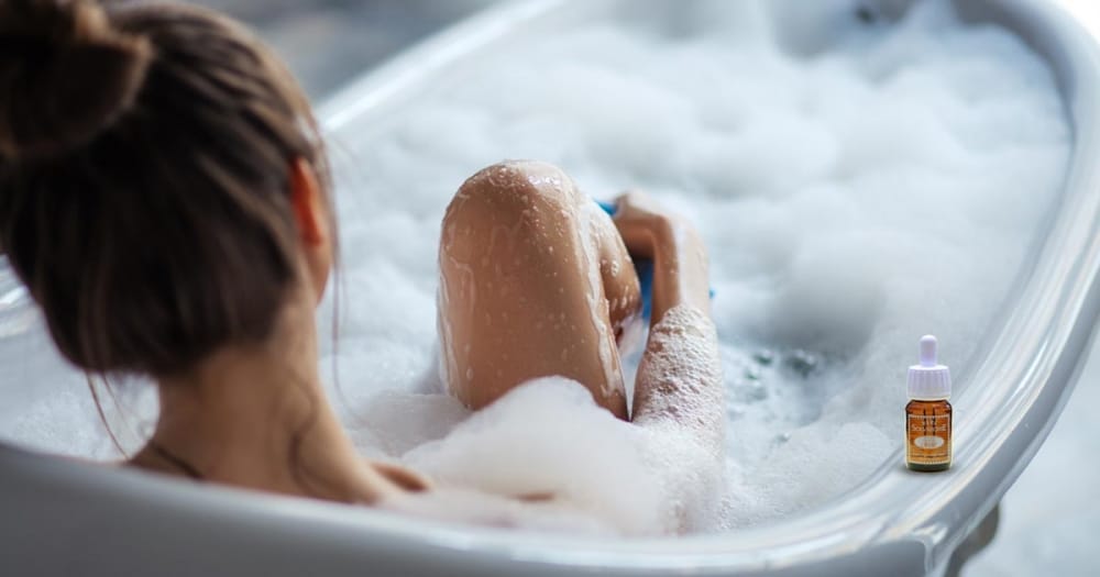 Femme qui se relaxe dans un bain avec un flacon d'huile essentielle posé sur le rebord de la baignoire
