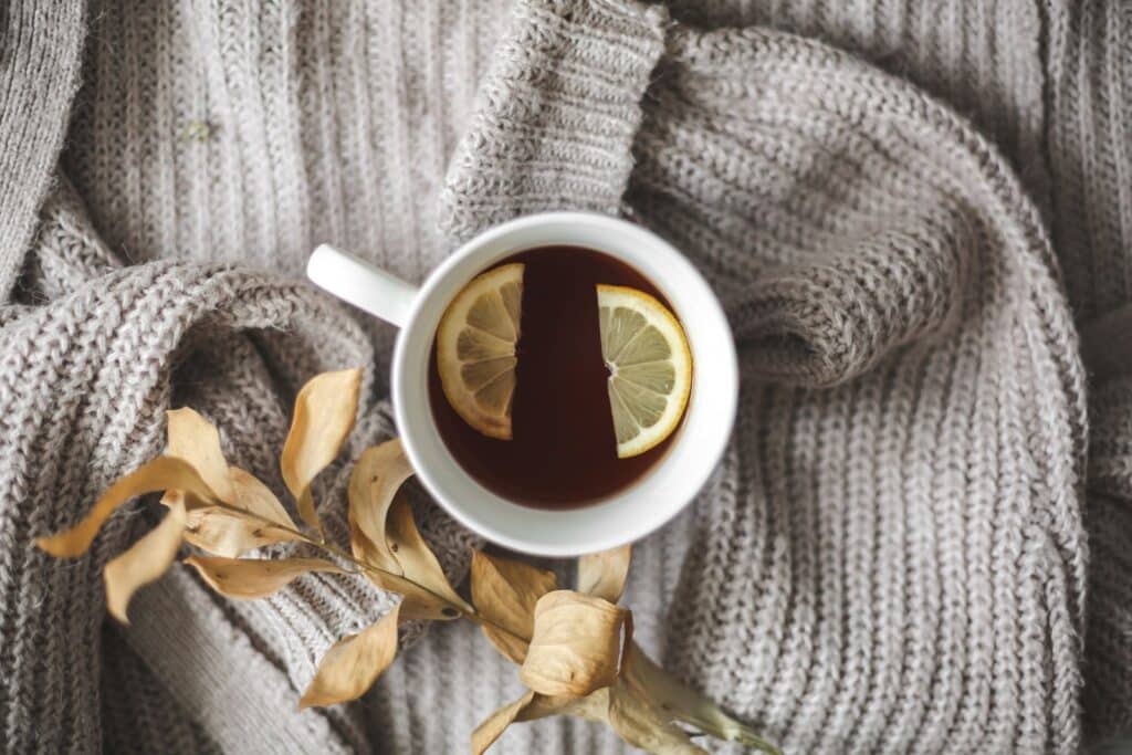Tasse de thé chaud au citron posée sur un pull en laine avec des feuilles séchées