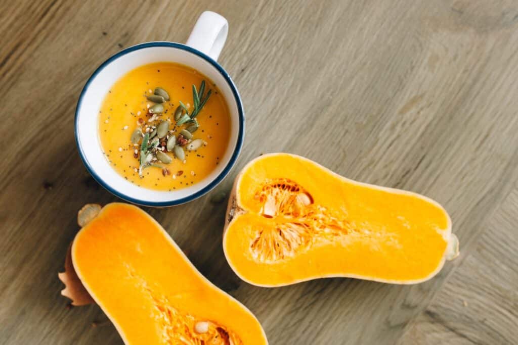 Velouté de butternut garni de graines et courge butternut coupée en deux sur une table en bois